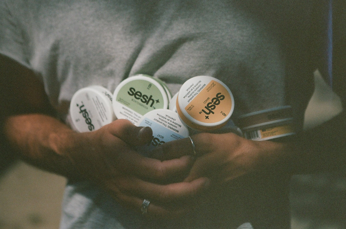 A person holding a handful of SESH+™ nicotine pouch cans.