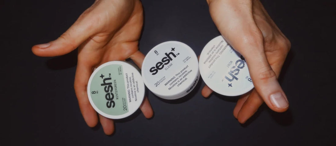 Hands holding SESH+™ nicotine pouch cans.